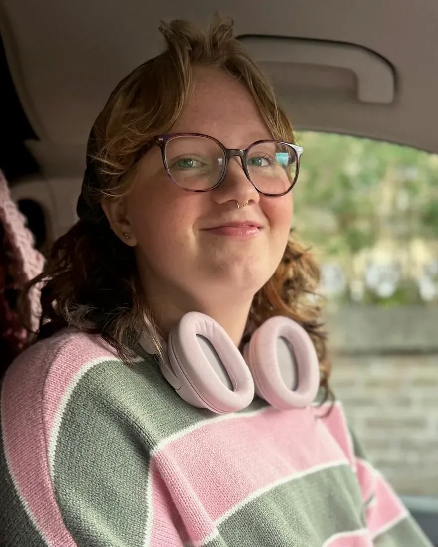 Eloise smiling, wearing glasses and a pink and green striped jumper